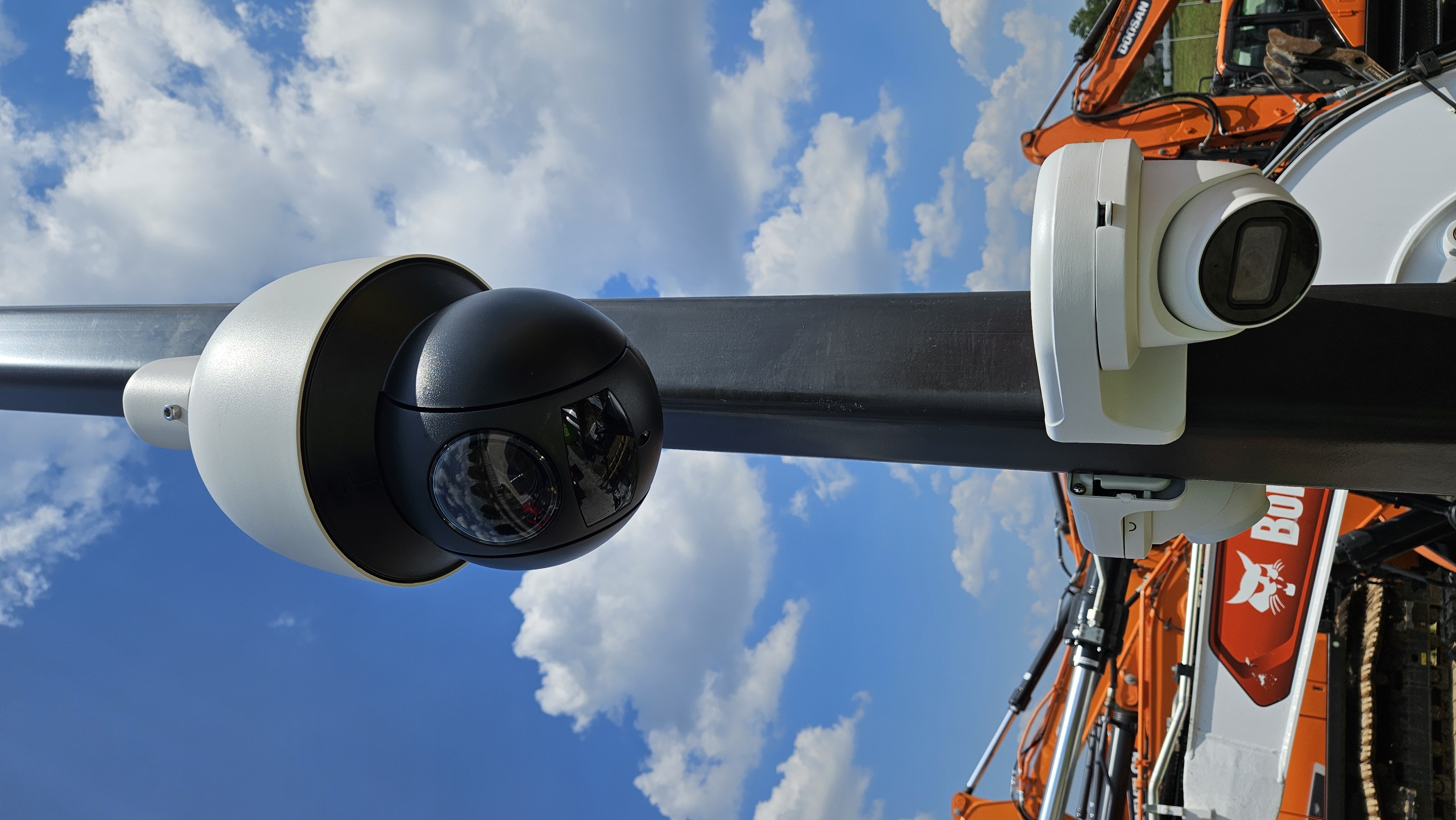 Close-up of PTZ dome and AI turret camera mounted on pole with heavy equipment in background